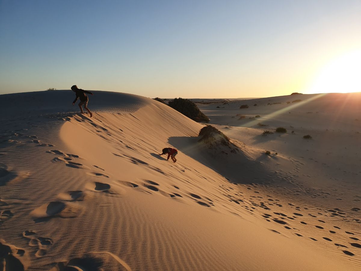 Two kids climbing a sand dune at sunset